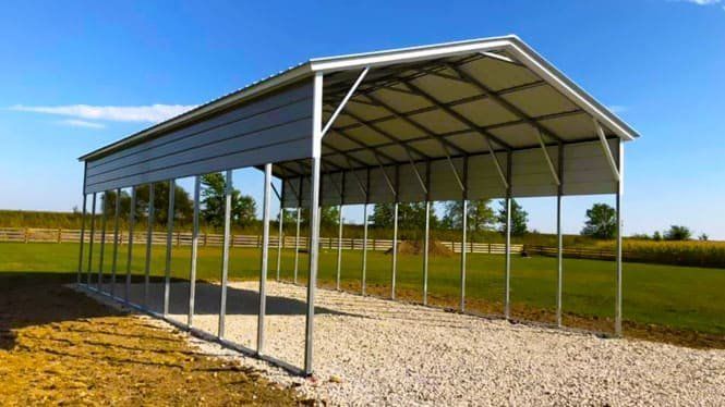 a metal carport is sitting on top of a gravel driveway in a field