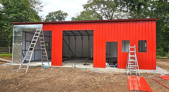A red metal garage is being built in the middle of a dirt field