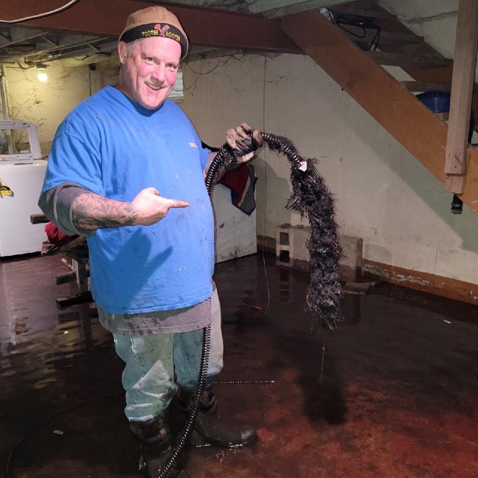 A person stands in a flooded basement, smiling while holding a large, dark mass of extracted roots or debris.