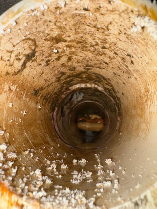 Rusty inside view of a cylindrical pipe with white mineral deposits and dark tunnel opening ahead