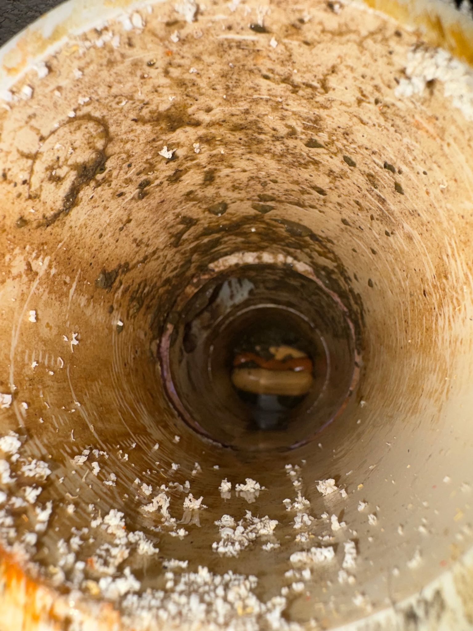 Rusty narrow pipe interior with white mineral buildup and a dark opening at the center