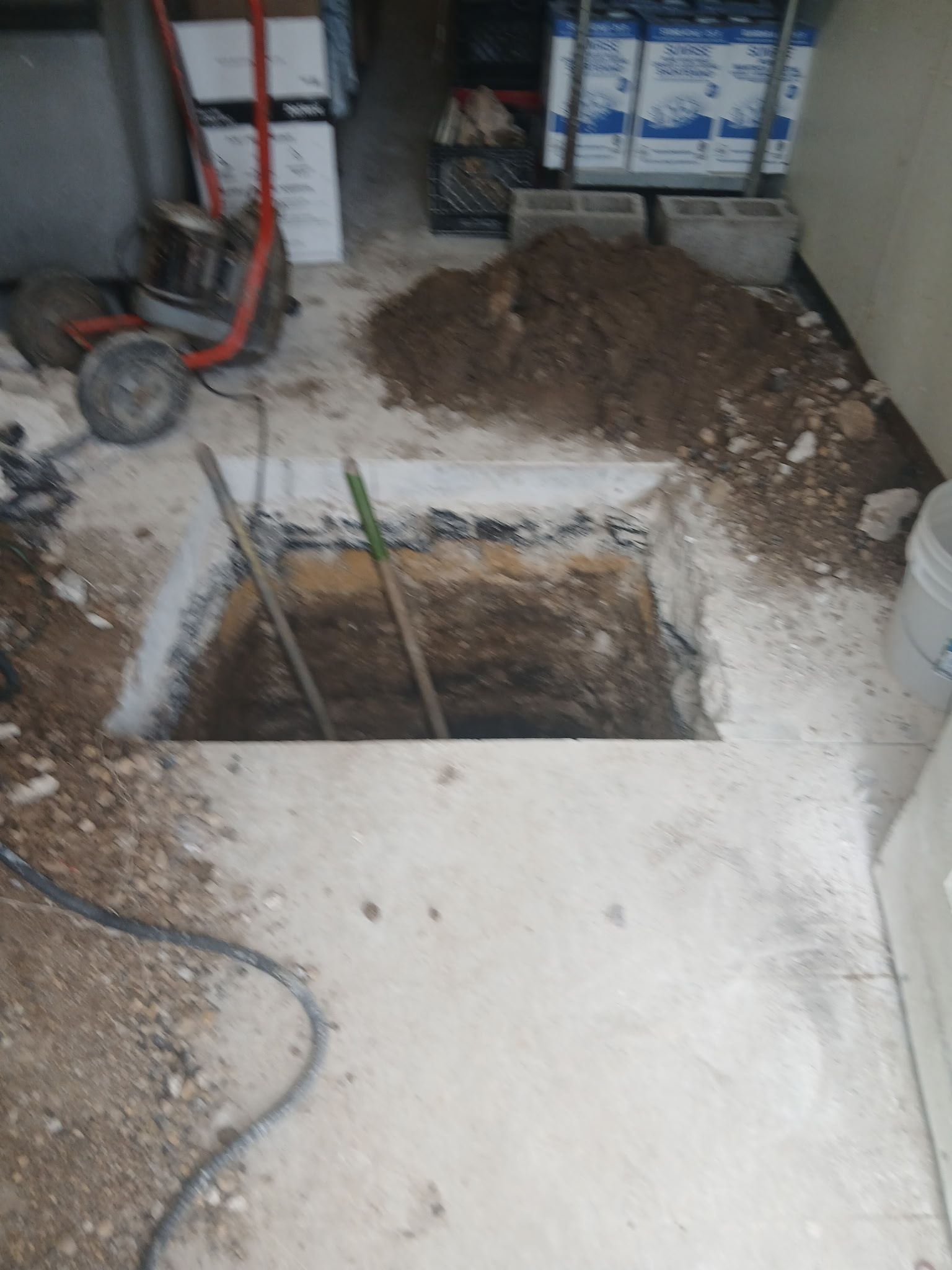 Open floor hole with exposed rebar and dirt pile in a basement or garage under renovation