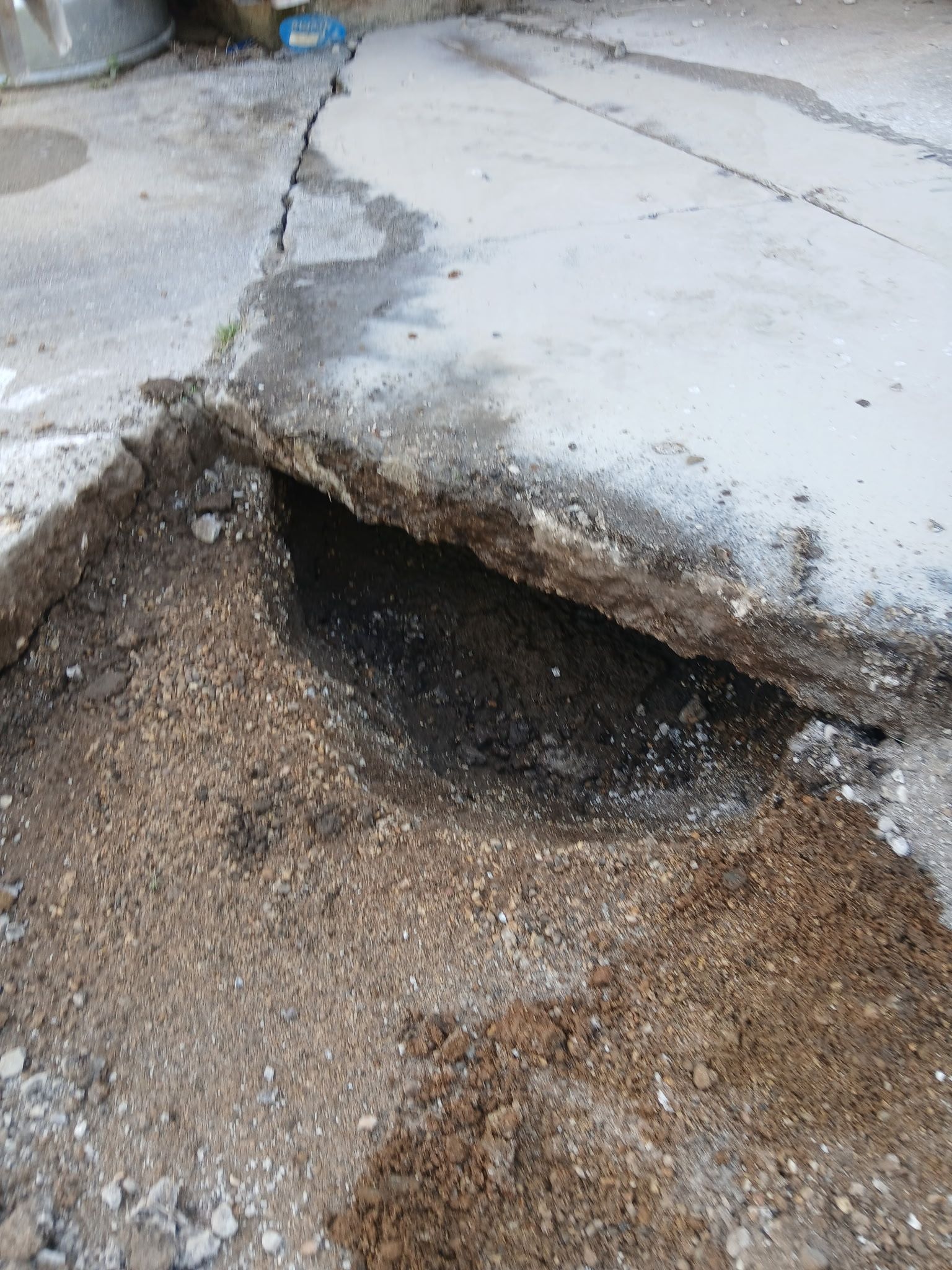 Cracked concrete road with a large sinkhole and exposed gravel beneath the broken edge