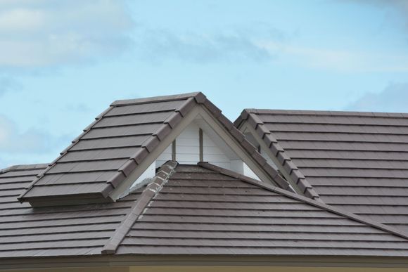 Brown tile roof with a triangular dormer against a cloudy sky.
