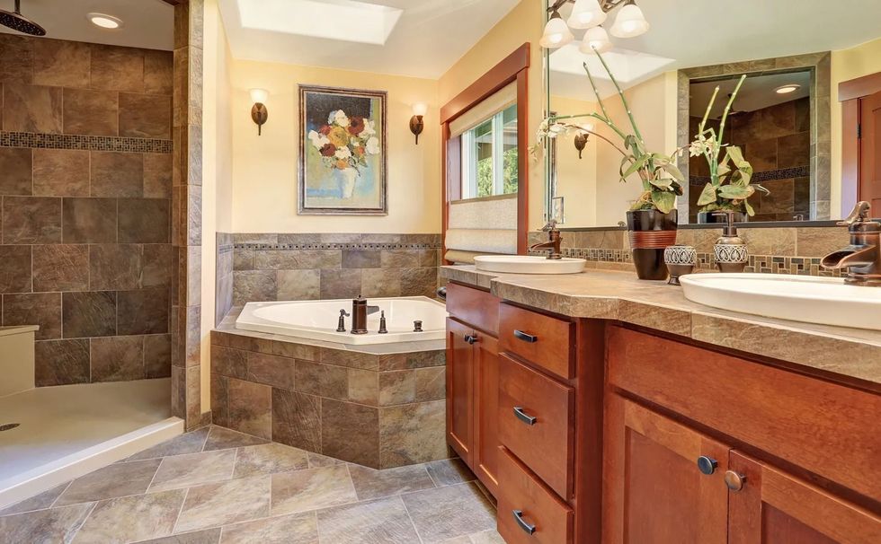 A spa-like bathroom featuring a tiled walk-in shower, a corner jetted tub, wooden cabinetry, and a large mirror.
