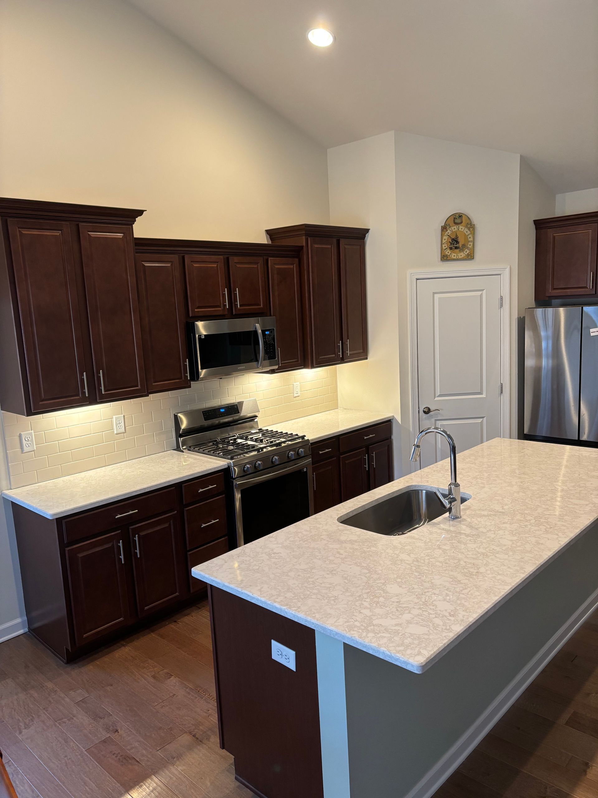 Kitchen with dark brown cabinets, stainless steel appliances, and a white countertop island.