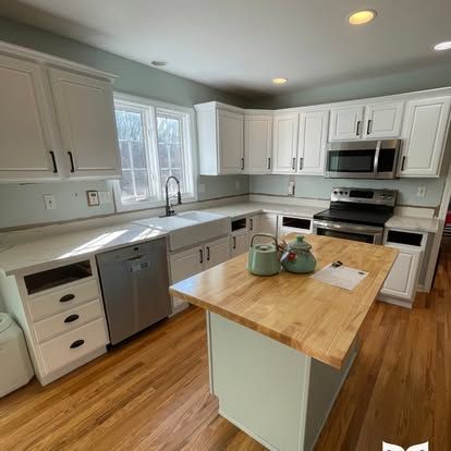 A kitchen with white cabinets , stainless steel appliances , hardwood floors and a large wooden island.