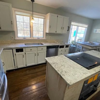 A kitchen with white cabinets , granite counter tops , stainless steel appliances and a large island.