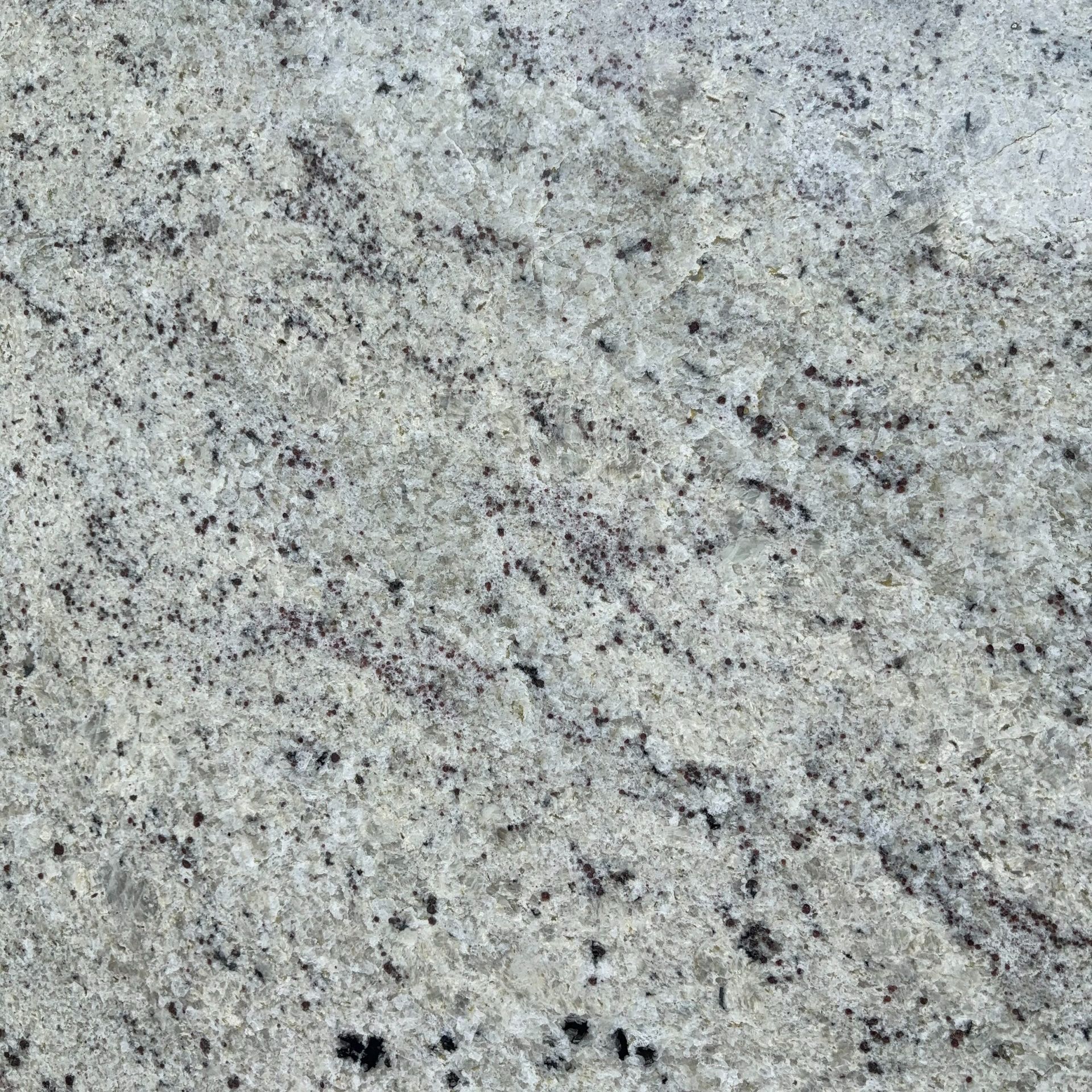 A close up of a white granite counter top with black spots.