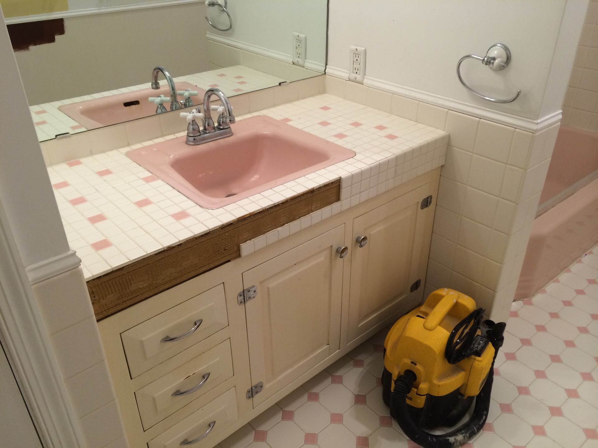 A bathroom with a pink sink and a yellow vacuum cleaner