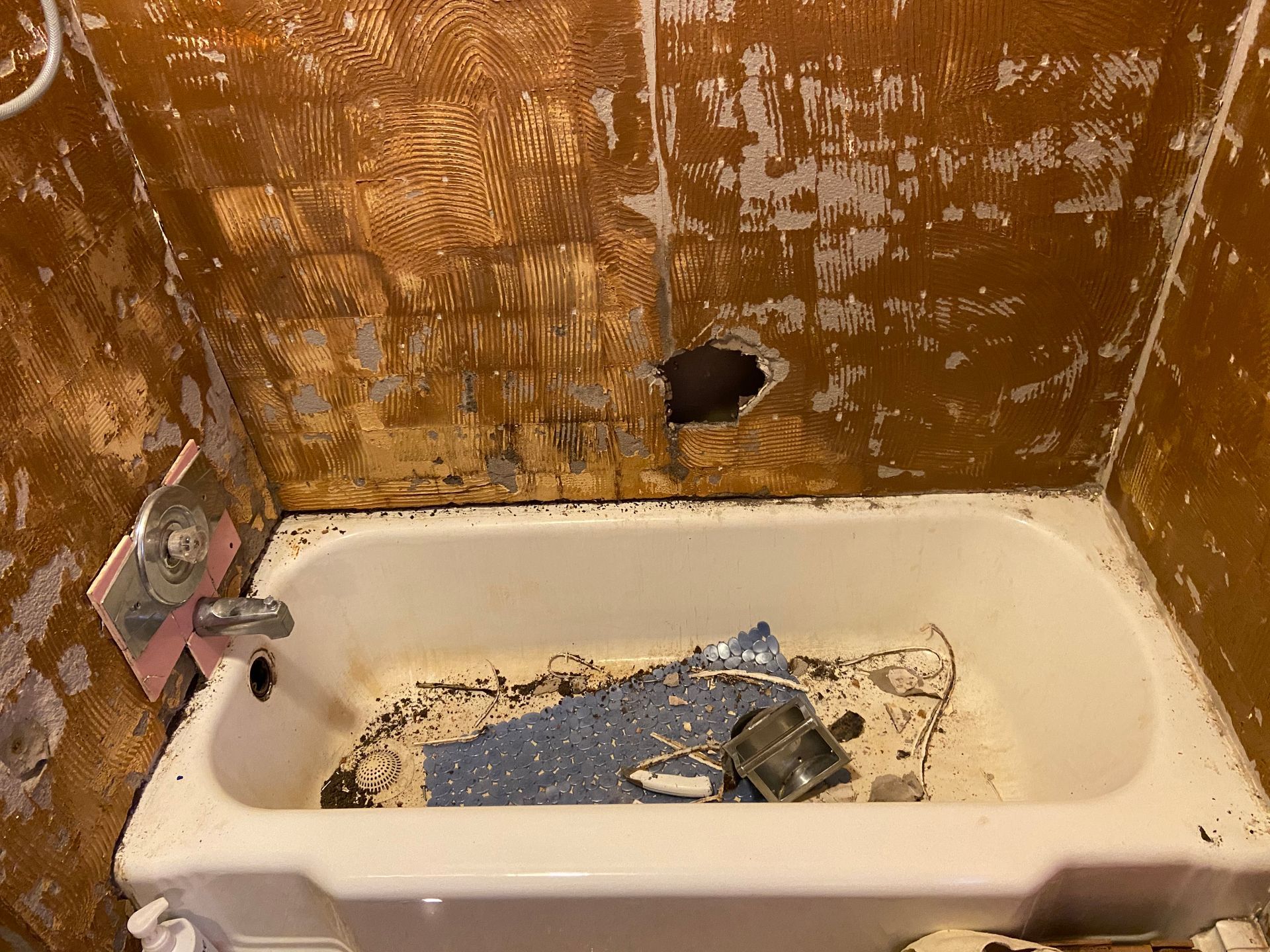 A bathtub in a bathroom with a hole in the wall