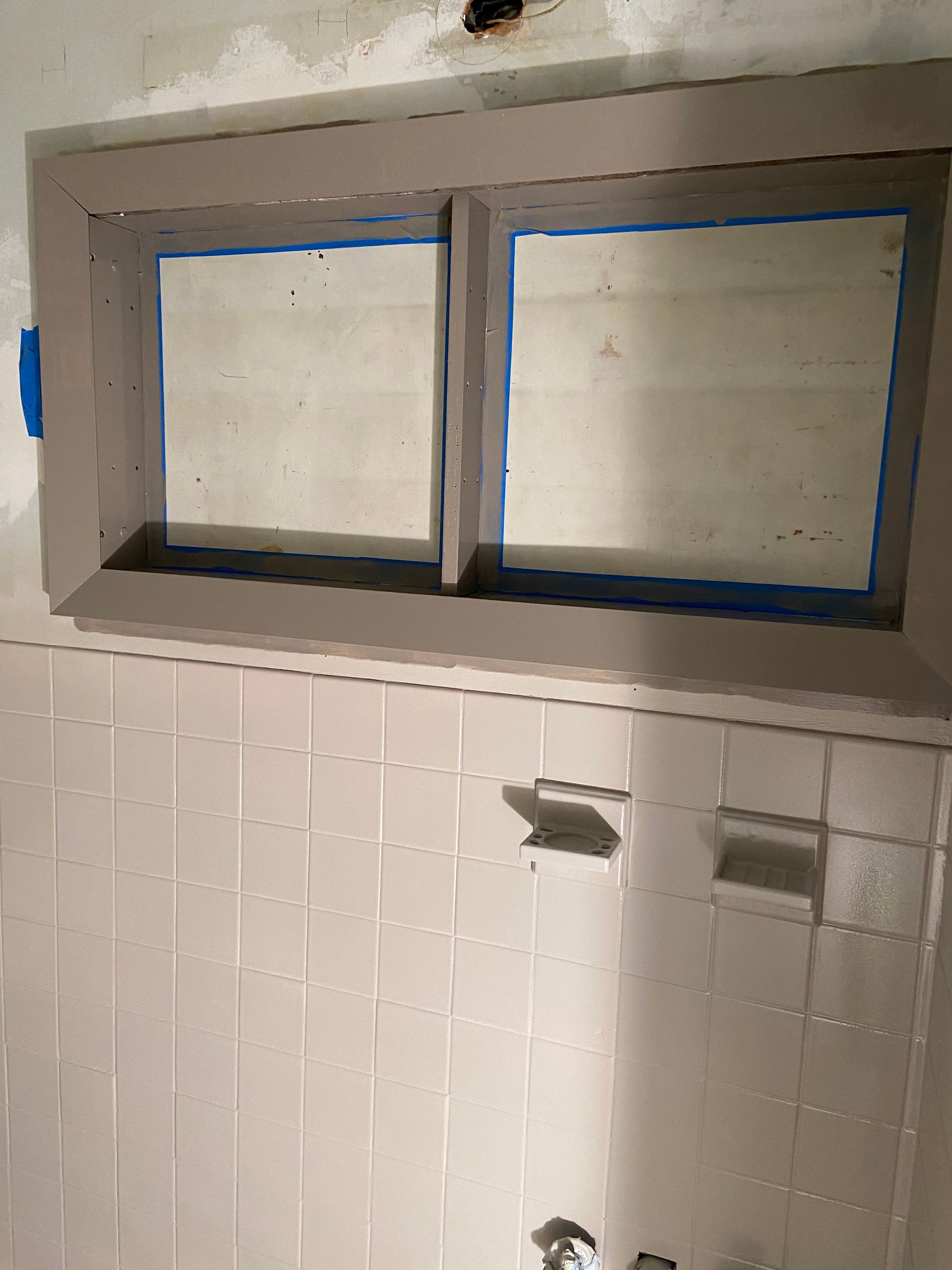 A bathroom with white tiles and a window with tape on it