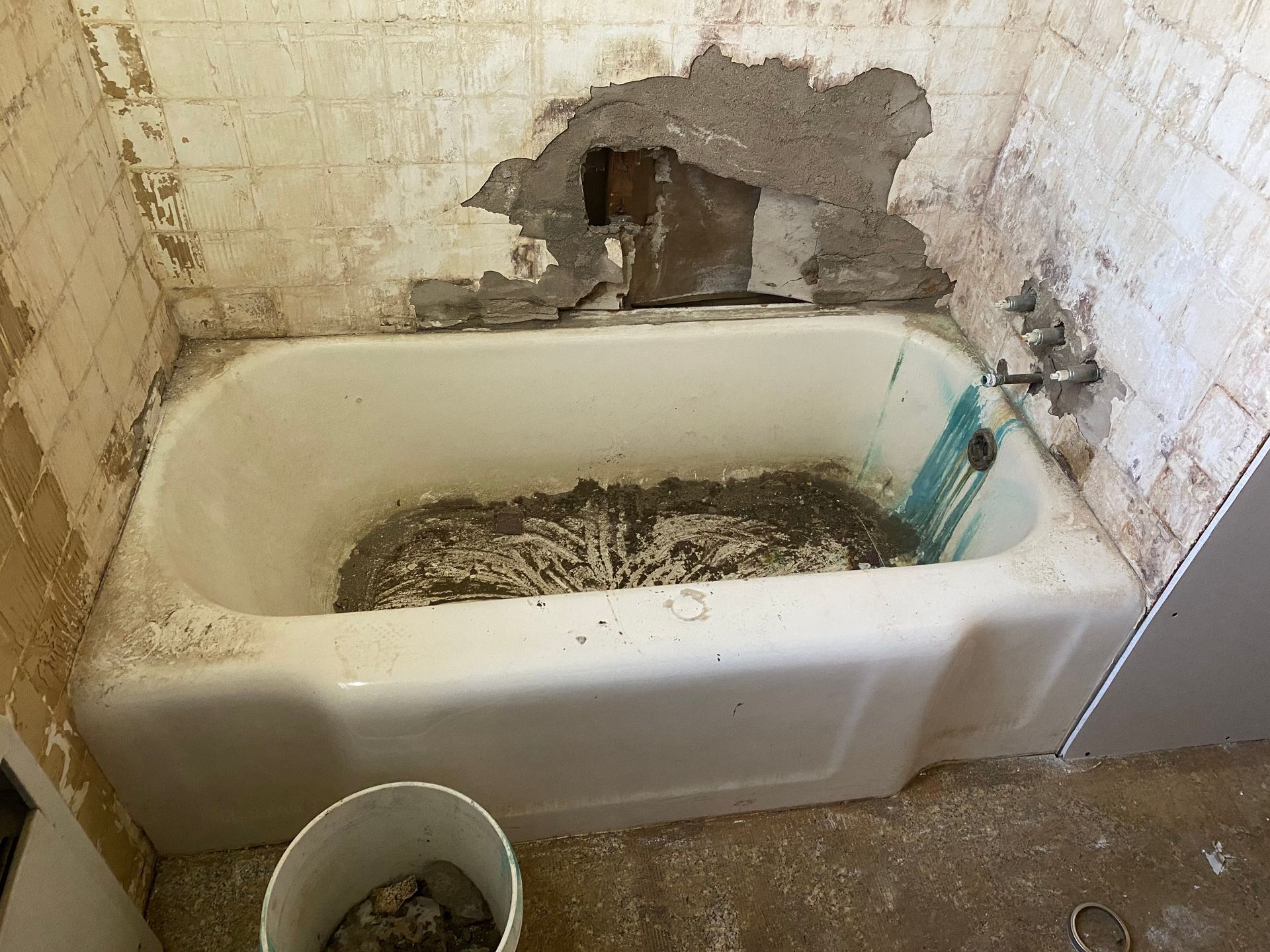 A bathtub in a bathroom with a hole in the wall