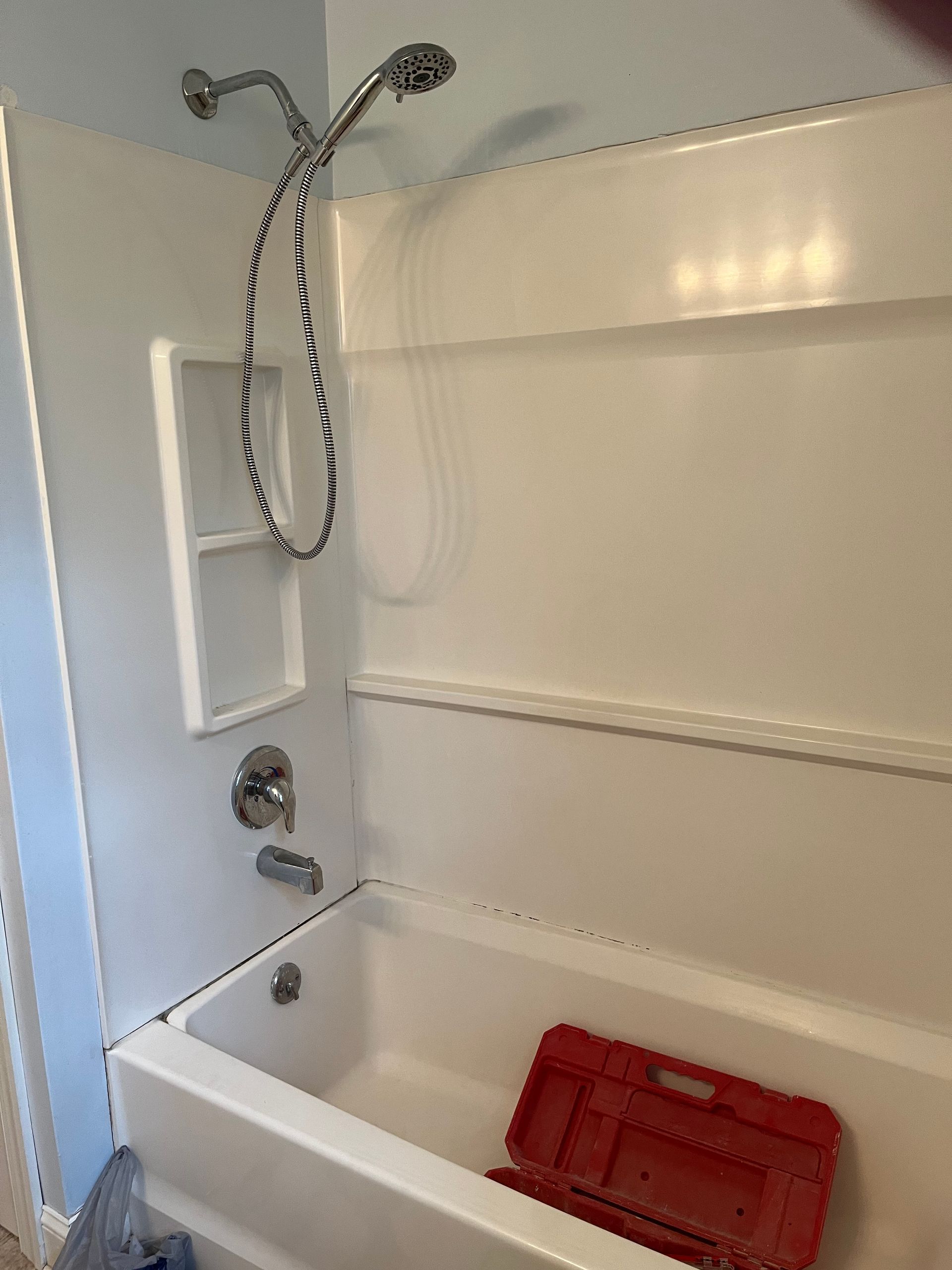 A bathtub with a shower head and a red toolbox in it