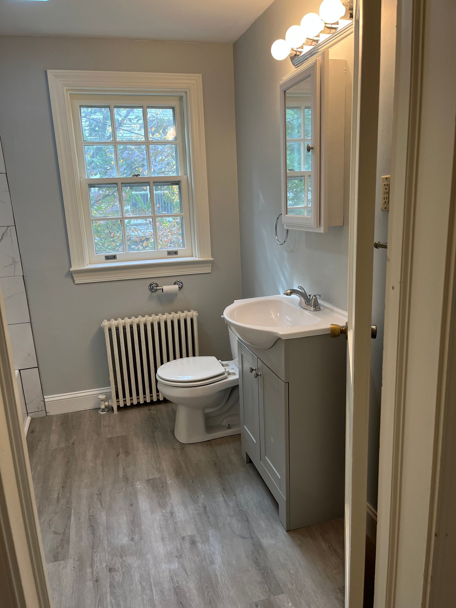 A bathroom with a toilet, sink, mirror and window