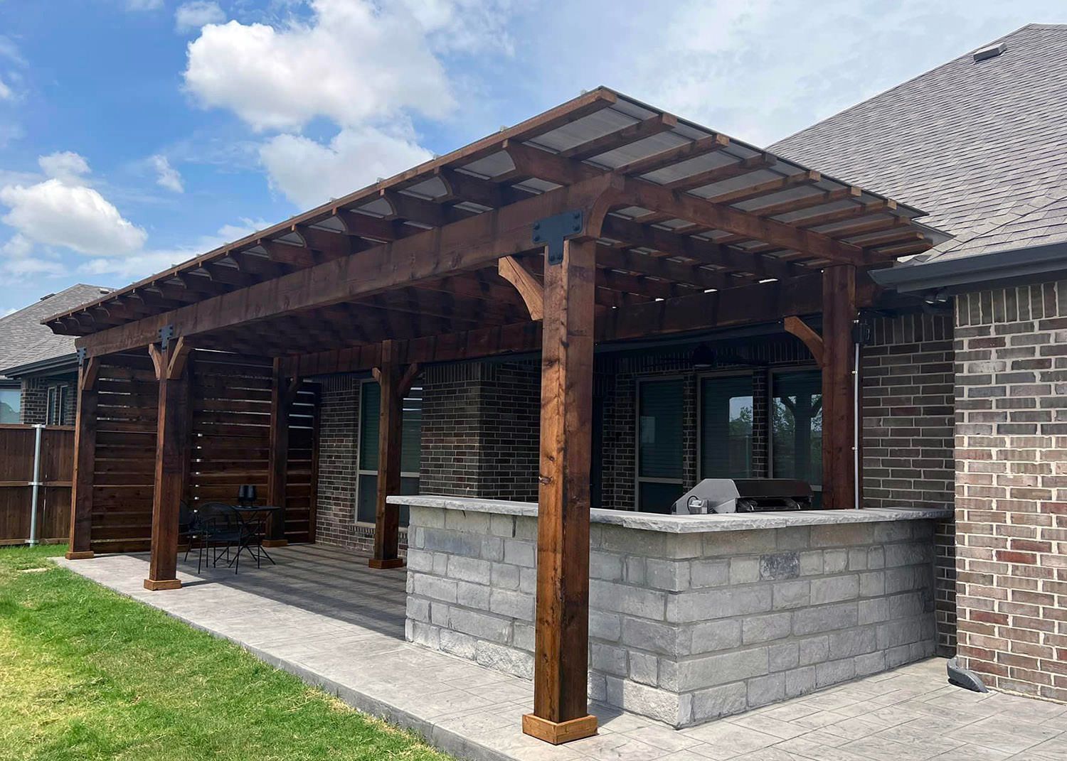 A wooden pergola is sitting on top of a brick patio next to a house.