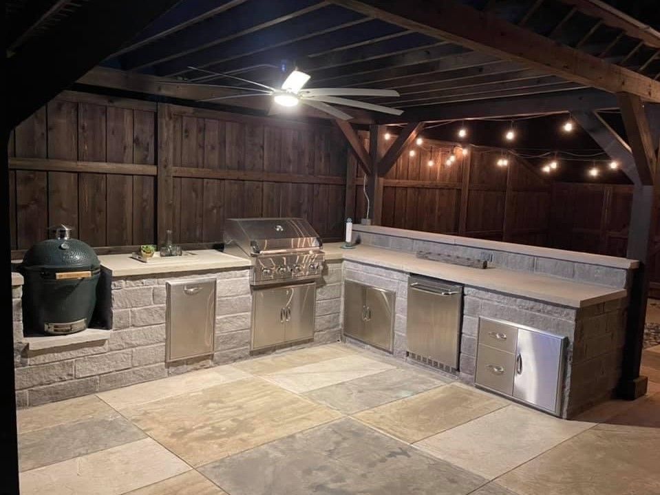 A large outdoor kitchen with stainless steel appliances and a ceiling fan.