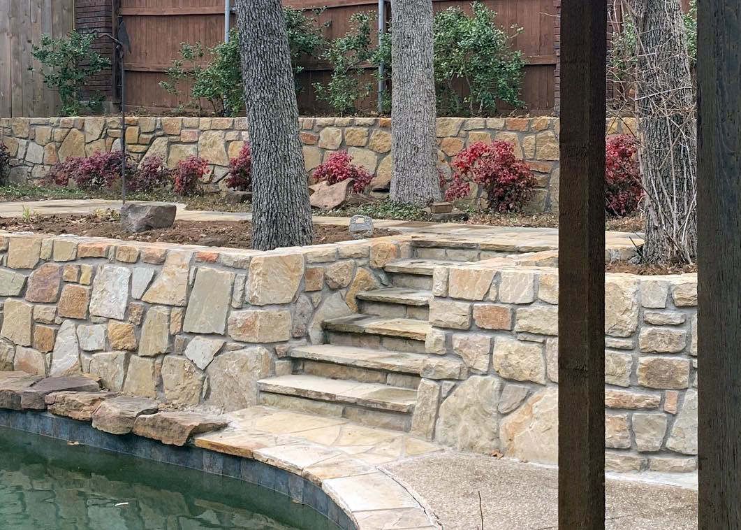 A stone wall surrounds a swimming pool with stairs leading up to it.