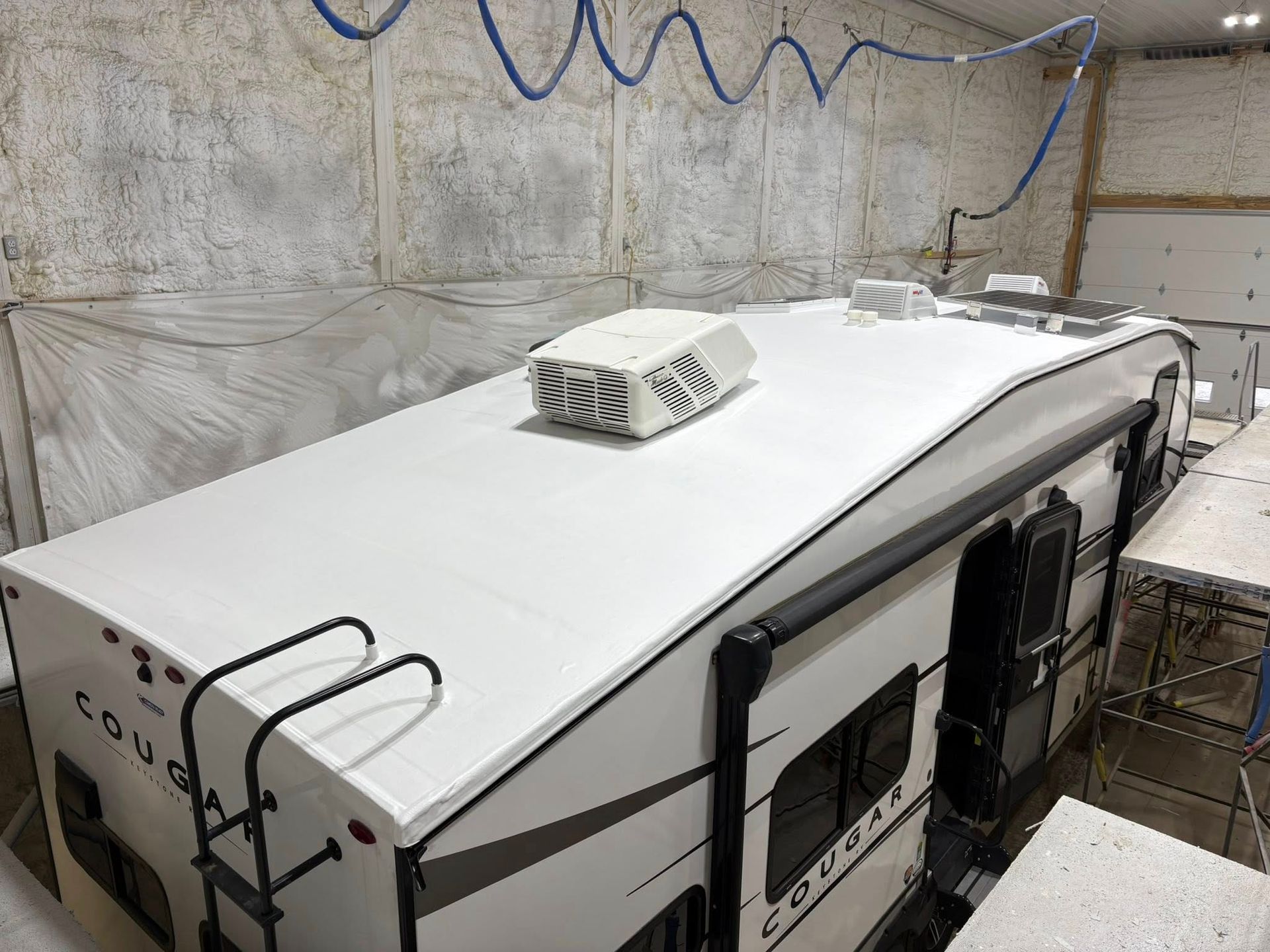 A white camper is being painted in a garage.