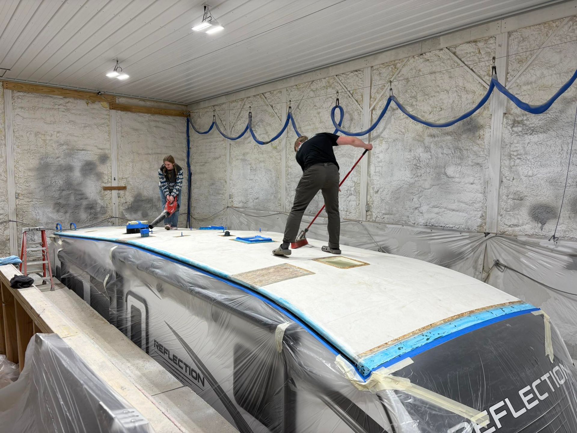 A man is painting the roof of a boat in a garage.