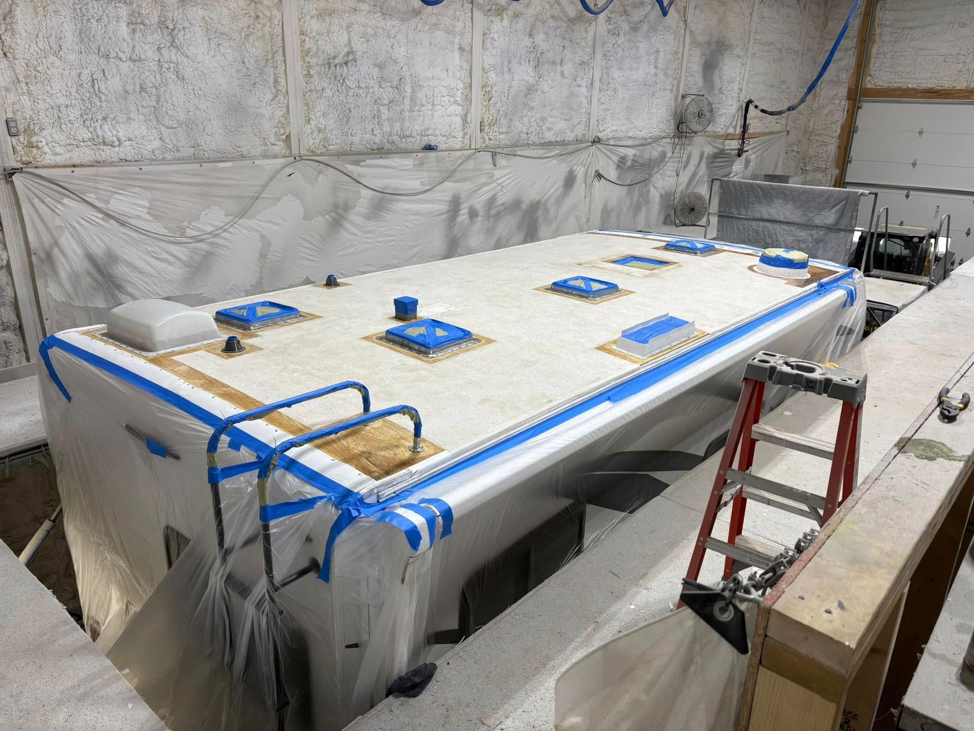 A large table with blue tape on it is sitting in a room with a ladder.