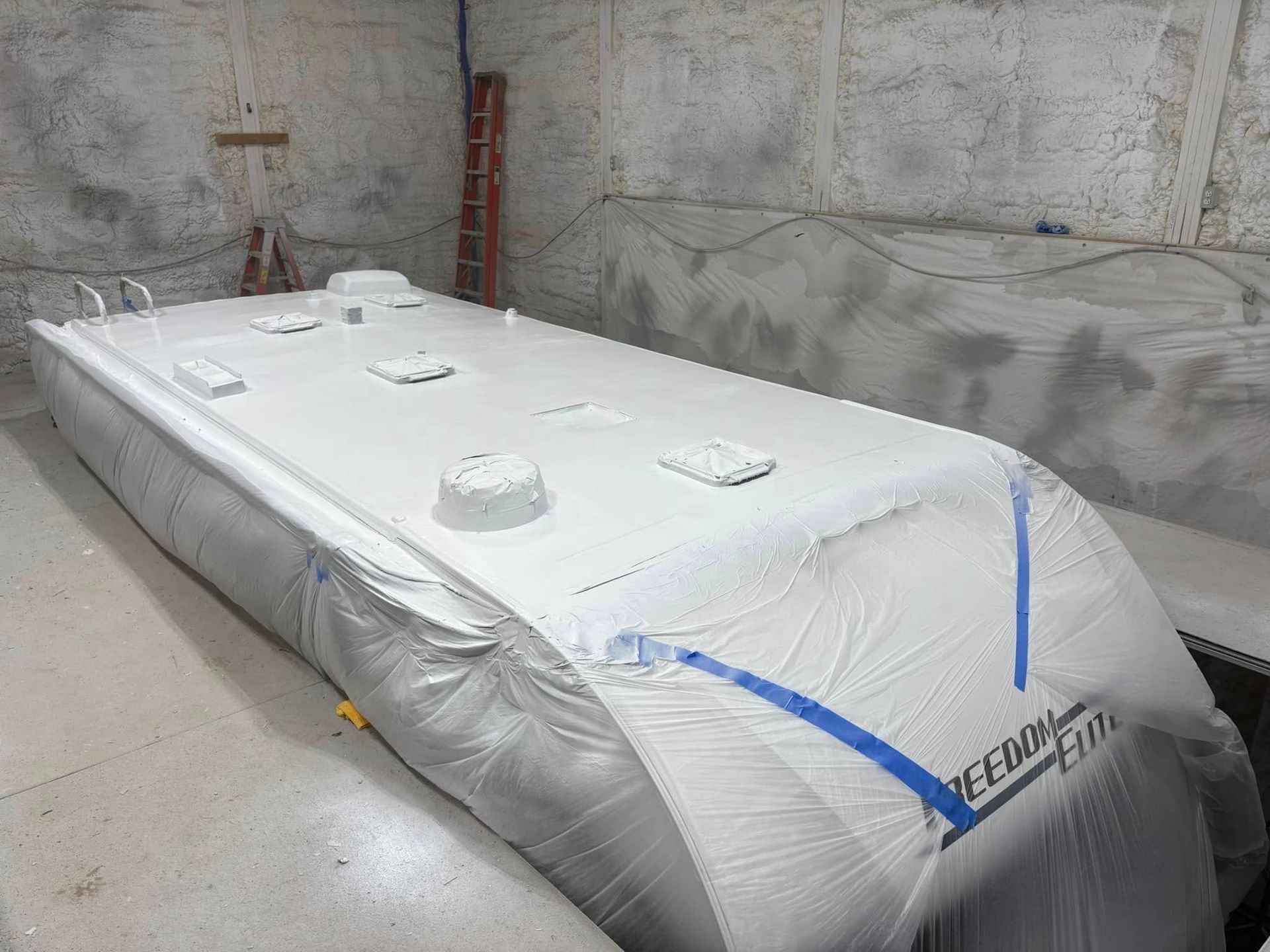 A boat is being painted white in a garage.