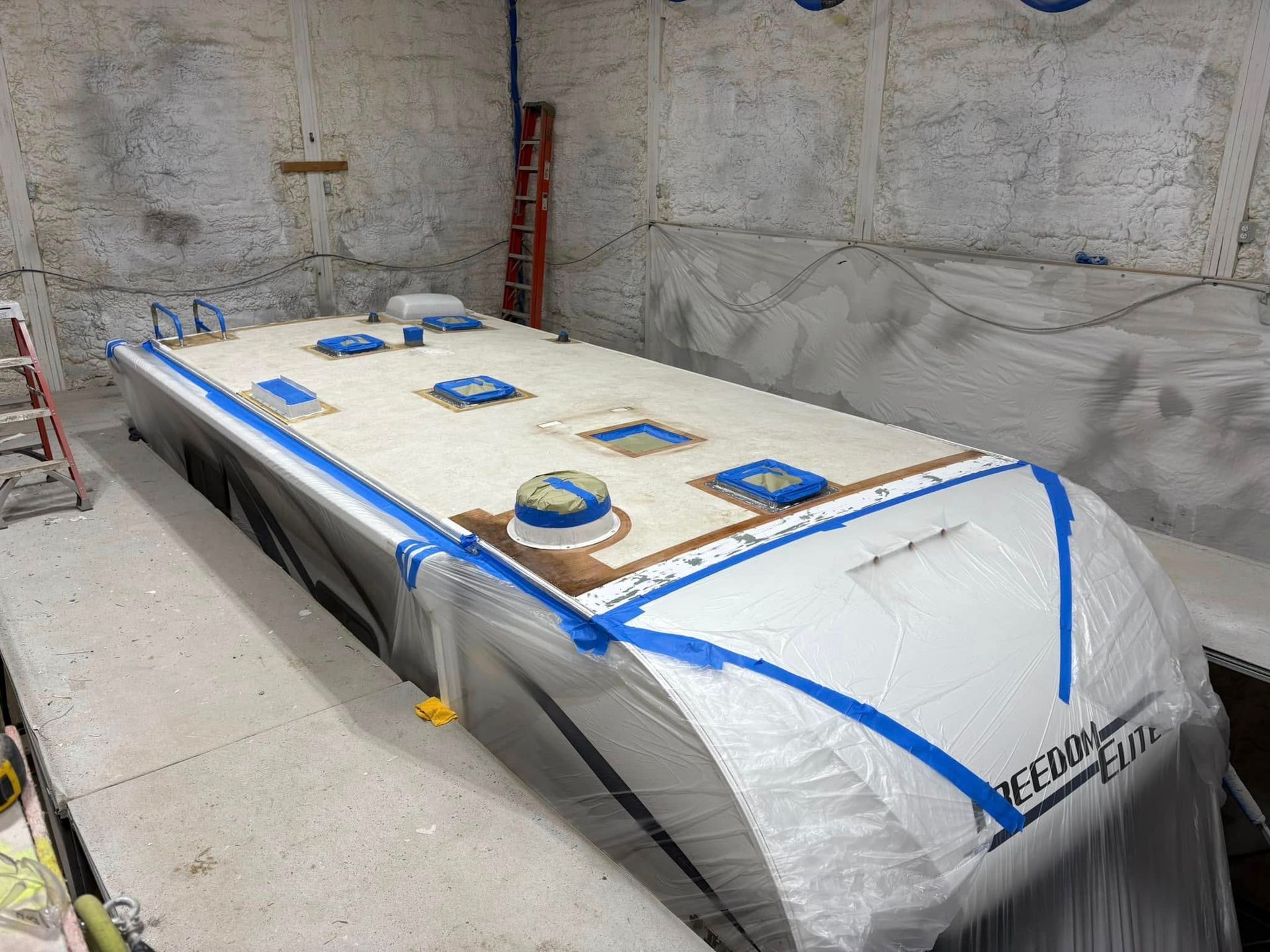 A boat is being painted in a garage with blue tape.