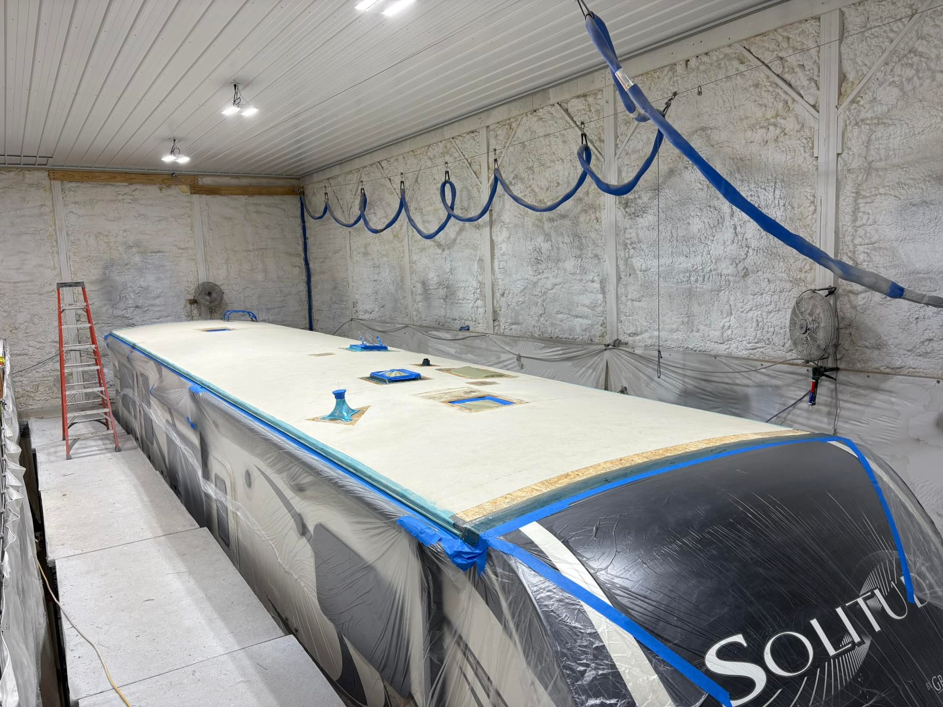 A boat is being painted in a room with a ladder.