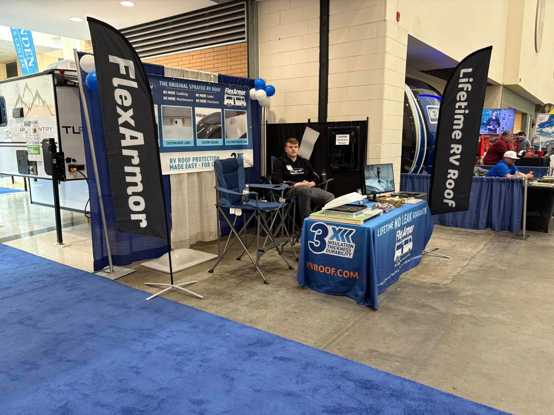 A man is sitting at a table in front of a flexarmor booth.