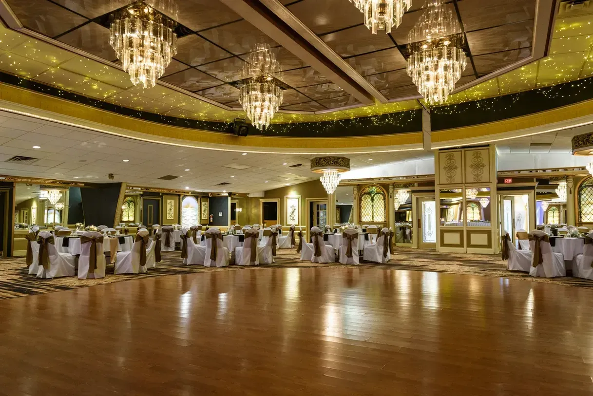 Ballroom with a wooden dance floor, round tables set for a formal event, and ornate chandeliers.
