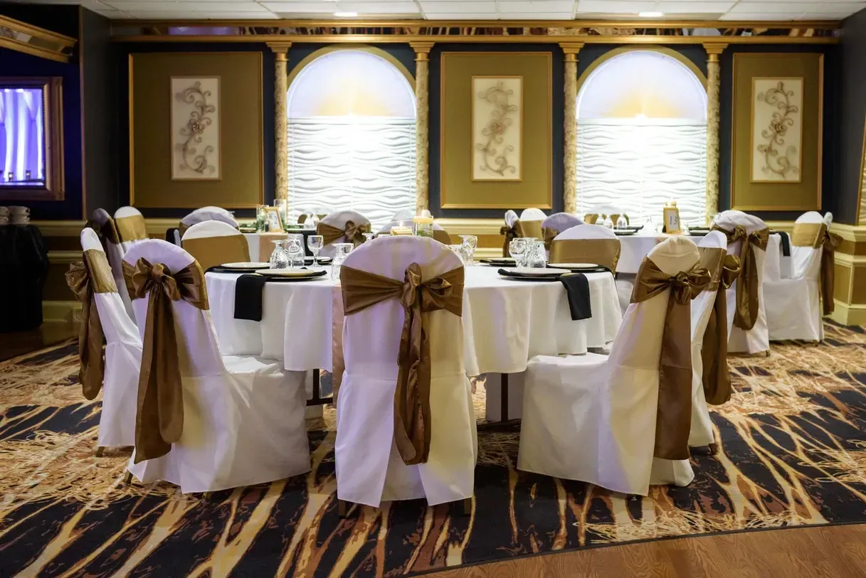Elegant banquet hall with round tables set for a special event. White linens and gold chair sashes create a luxurious feel.