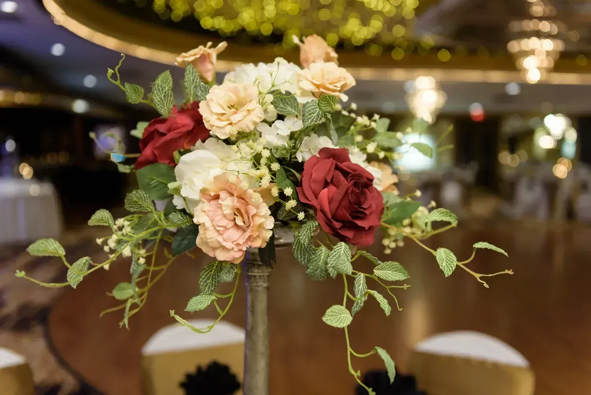 Floral centerpiece with red, peach, and white blooms on a tall, metal stand at a formal event with blurred background.