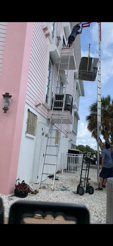 Workers using a lift to access a building's upper levels; a pink and white building with a flag.