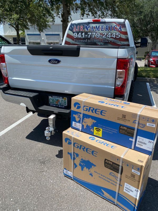 White Ford truck with two Gree air conditioner boxes in a parking lot.