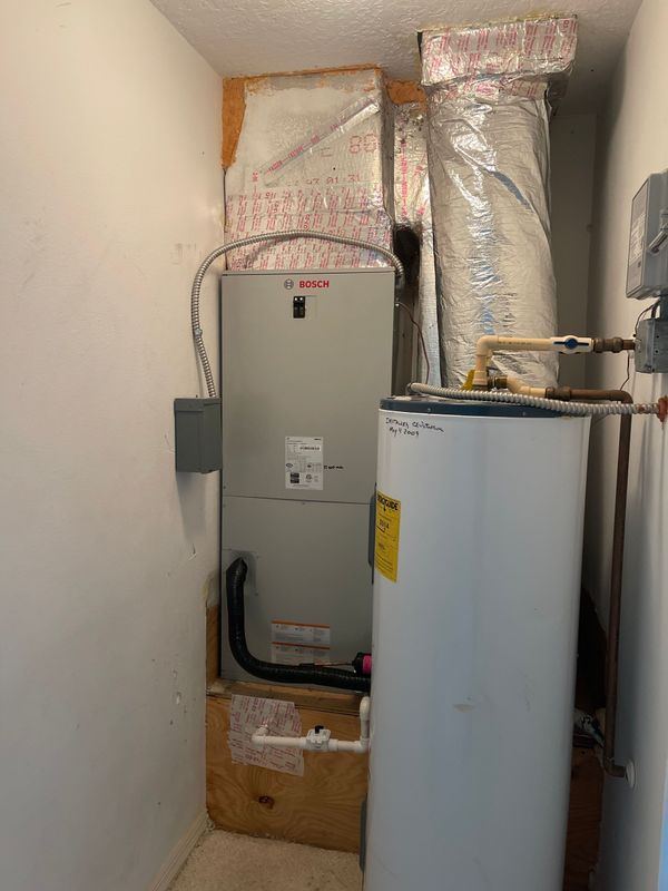 HVAC unit and water heater in a small utility closet. Ductwork and electrical components are visible.