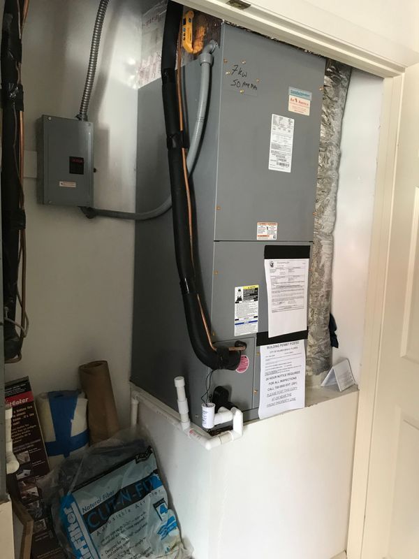 HVAC unit in a closet. Gray metal unit with black insulated lines, white base, and papers attached.
