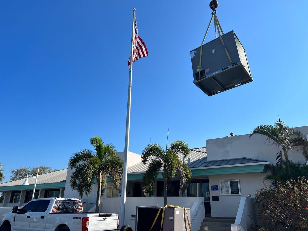 A crane lifting an HVAC unit above a building with an American flag on a sunny day.