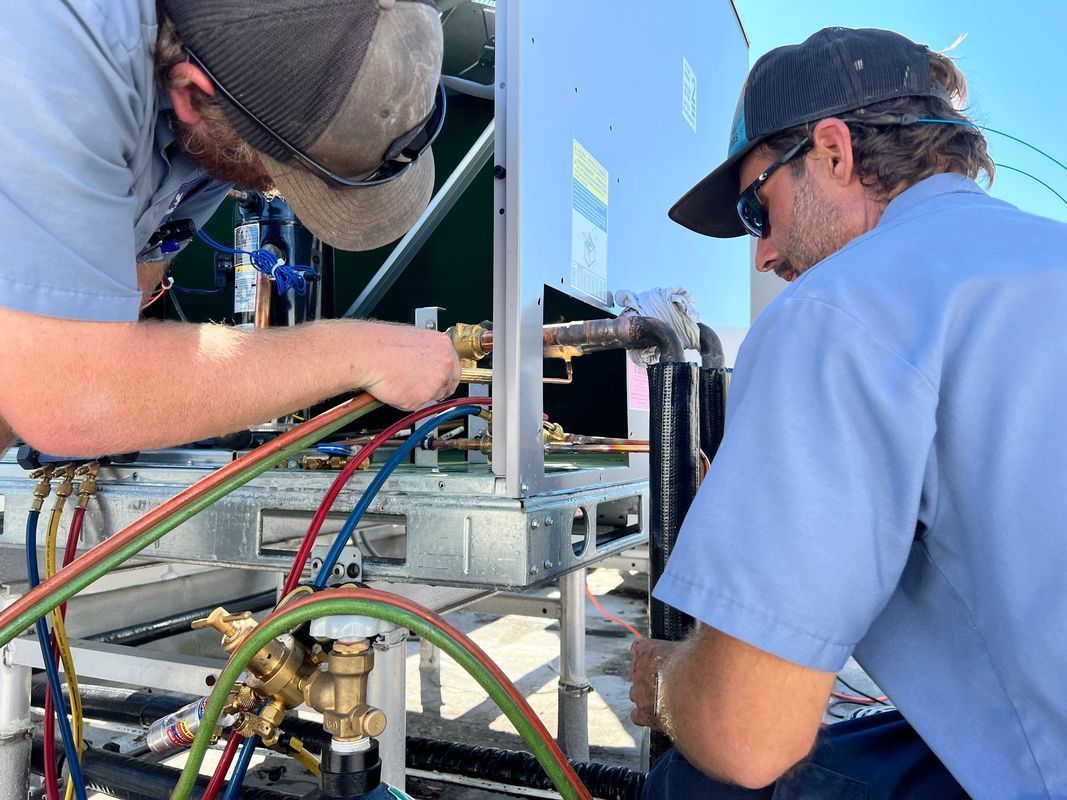Two HVAC technicians working on outdoor equipment, using torches.