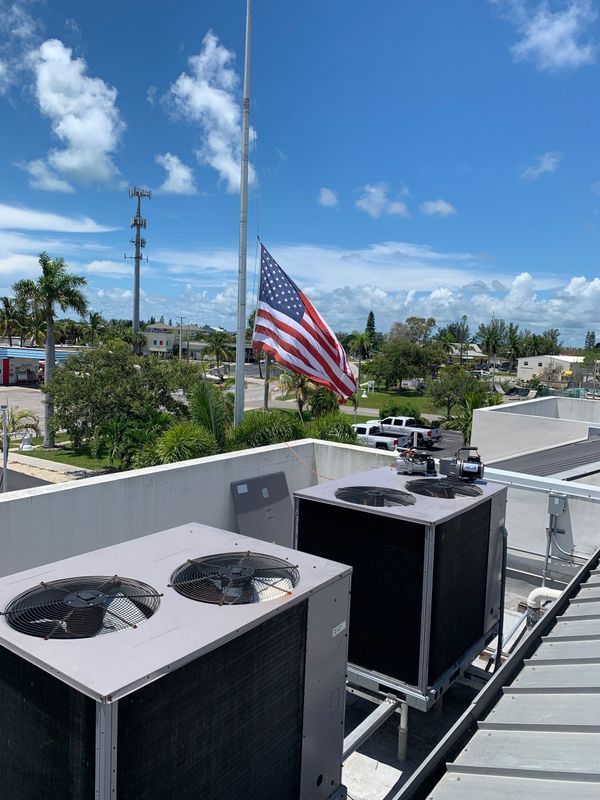 Rooftop with air conditioning units, American flag at half-mast under a partly cloudy sky.