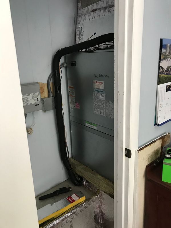 HVAC unit in a small room, with black insulation, gray unit, and exposed wiring.