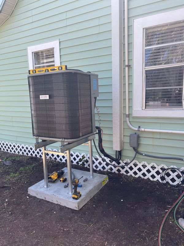 AC unit on a concrete pad with supporting metal frame, beside a light blue house.
