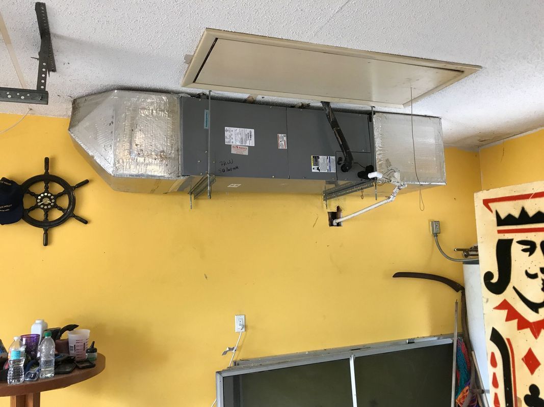 HVAC unit mounted on yellow wall in a room, with access panel in ceiling.