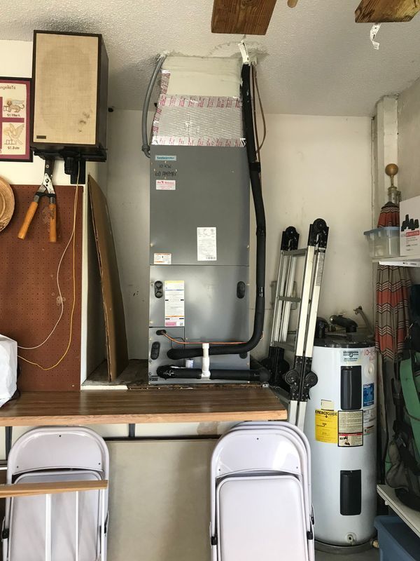 HVAC unit and water heater in a garage setting with folding chairs, tools, and storage.