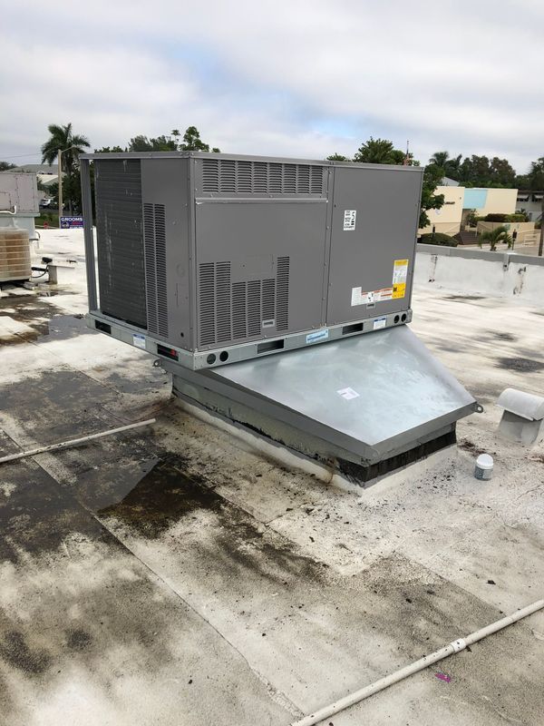 HVAC unit on a flat roof, elevated on a metal frame, with a cloudy sky in the background.