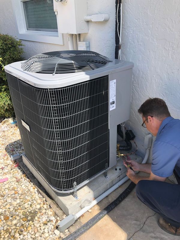 A man in a blue shirt works on an air conditioning unit outside a building.