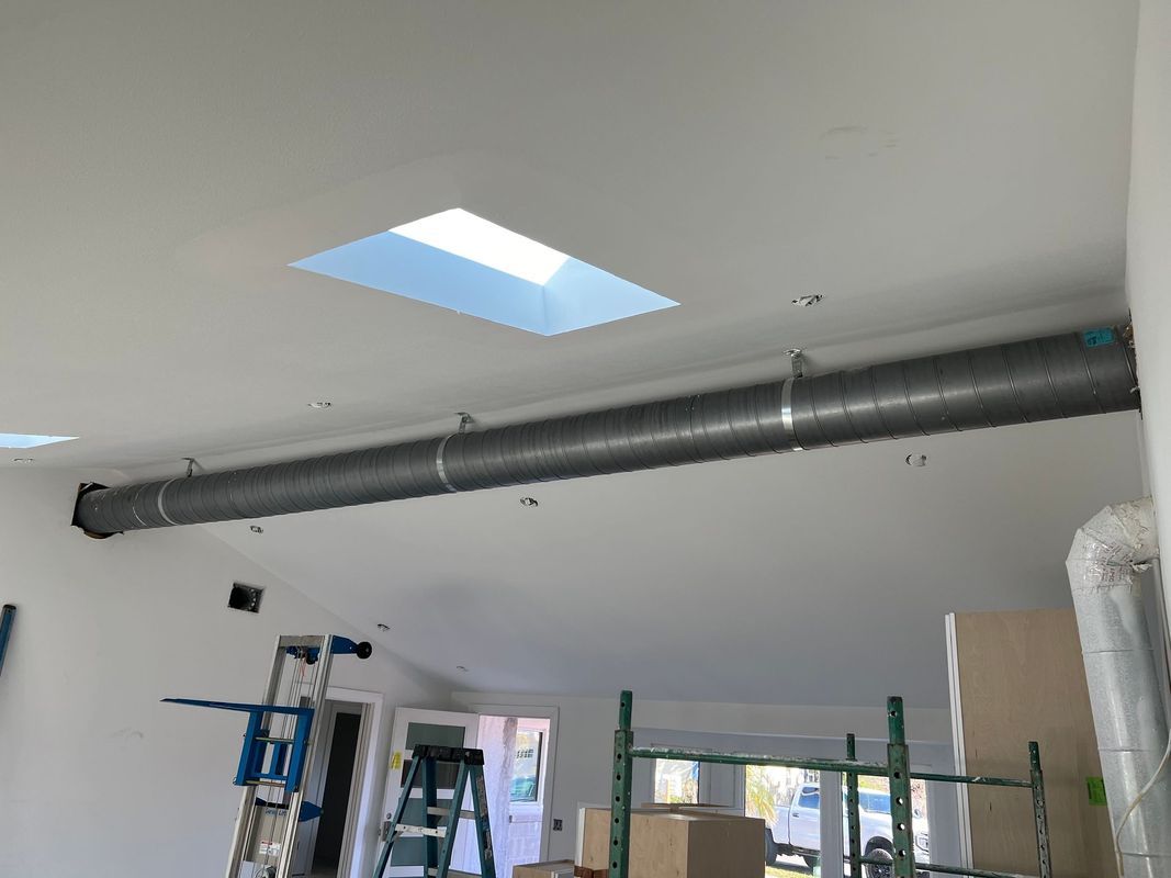 Galvanized HVAC ductwork runs across a ceiling with a skylight and construction equipment visible.