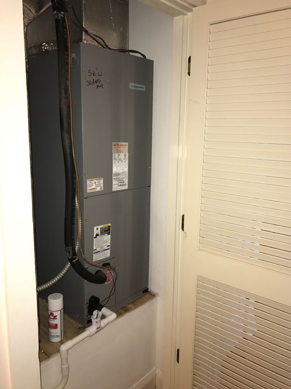 HVAC unit in a closet. Gray metal box, black flexible tube, white drain pipe, and a partially open door.