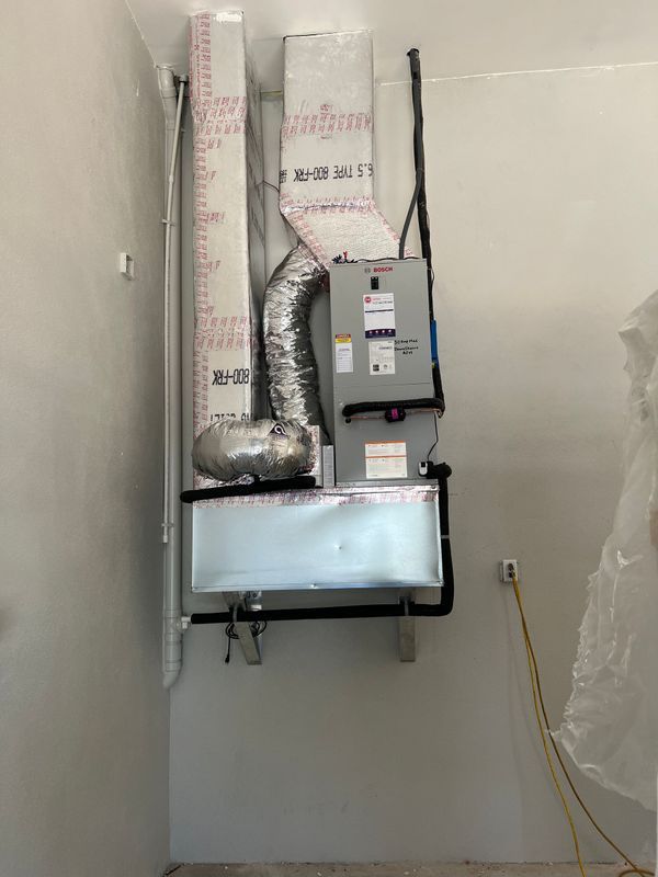 HVAC system installed in a corner. Ductwork, furnace, and a/c unit on a light gray wall.