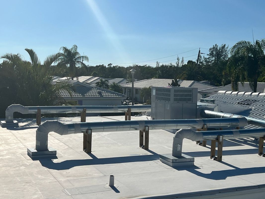 Rooftop with HVAC equipment and insulated metal pipes under a blue sky, surrounded by trees.