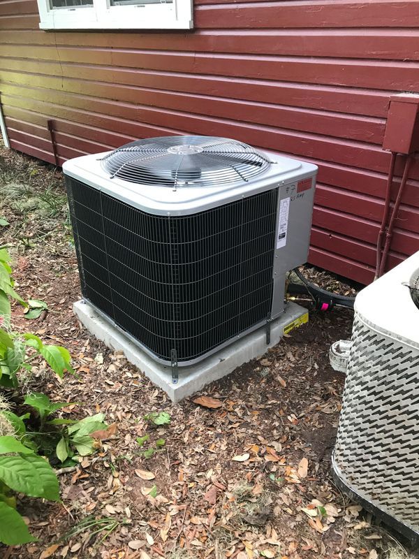 Outdoor air conditioning unit next to a building with red siding.